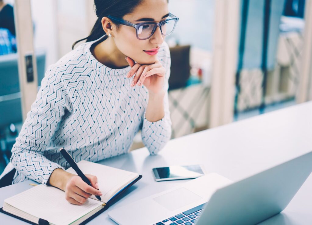 Woman on laptop writing in notebook